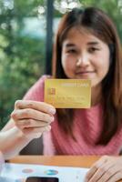 Woman displaying a gold credit card, emphasizing finance and banking themes, with a natural green backdrop. photo