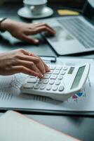 Close-up of hands using a calculator and laptop, analyzing financial data in a modern office environment. photo