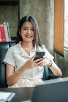 A young woman with a smartphone, smiling in a modern office environment, conveying professionalism and connectivity. photo