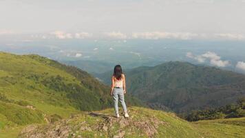 Young beautiful caucasian georgian woman standing on Gomis Mta mountain top viewpoint enjoying panoramic view over green valleys, dramatic landscape of Caucasus region in summer season. video