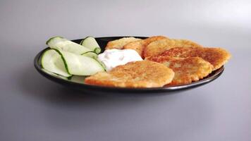 Potato pancakes with sour cream and cucumber on a black plate. video