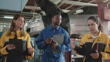 Latino female inspector works on service checklist of car fix, with multiracial maintenance mechanics team at a garage, professional engineer worker jobs in auto and transportation industry business. video