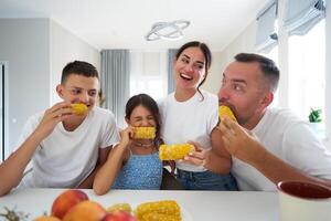 Family enjoying corn on the cob at a bright kitchen table during a casual summer gathering photo