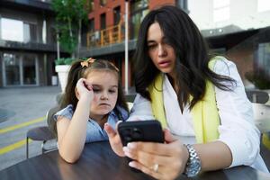 Mother and daughter enjoying time together while looking at a phone outside a modern building on a sunny day photo