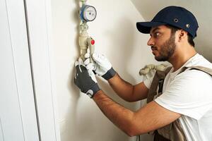 Professional male plumber in uniform is fixing water meter with special work tools at home photo