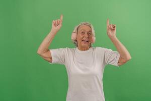 A Joyful Senior Woman is Dancing Happily with Earmuffs on a Bright Green Background photo