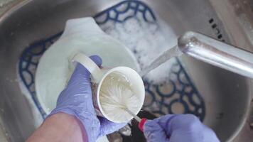 A hand in a blue glove washes a cup with a brush under running water in a sink with suds video