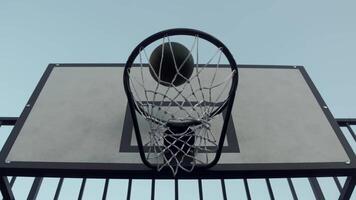 Close-up of a basketball hoop, with a basketball rebounding off a backboard in an outdoor arena, under a clear blue sky. team gets a point. Slow motion video