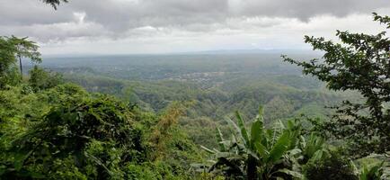 Lush Green Hilltop Panorama Stunning View of Distant Village and Rolling Hills under a Cloudy Sky photo