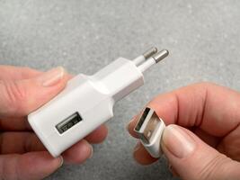 The woman's hands connect or disconnect the USB cable and AC power adapter. AC power charger with USB connectors. AC charger, adapter with USB input photo