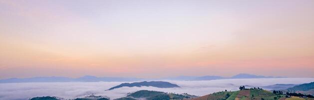 Breathtaking mountain panorama with dense white fog and clouds at dawn featuring soft pastel sky colors creating peaceful natural landscape perfect for travel tourism and wellness marketing materials photo