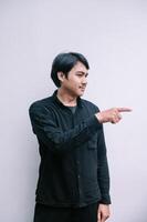 An Asian Man in a Black Shirt Pointing Towards Blank Space for Message photo
