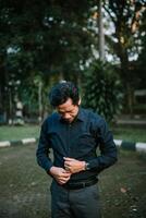 Formal asian man in park preparing for work attire buttoning shirt photo