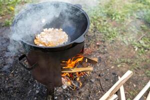 Cooking Traditional Dish Over Open Fire With Cast Iron Pot in a Rural Outdoor Setting During Daylight photo
