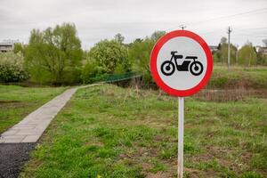 Motorcycle Prohibited Sign Near a Walking Path by a River in a Green Area on a Cloudy Day photo