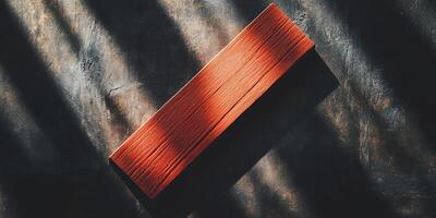 A close up shot of a red wooden block on a textured dark surface with light and shadow patterns around it photo