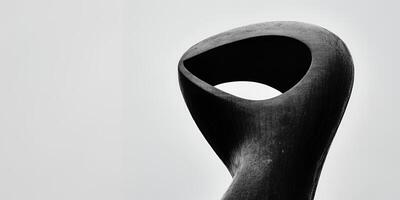 Close up of a dark abstract sculpture with a hole against a light background in a minimalist style photo