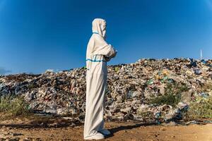 Man in bacteriological protective suit watching to the landfill. Environmental pollution issue photo
