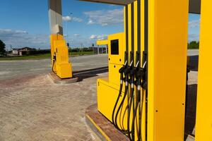 The fuel pumps, painted bright yellow, are situated at a deserted gas station under a clear blue sky, with lush green fields visible in the background on a sunny day photo