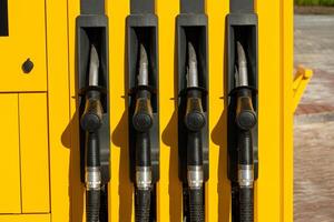 Four pump nozzles are lined up at a gasoline station, showcasing a bright yellow design against a clear daytime backdrop. The area is well-lit and inviting photo