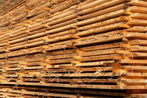 Wooden planks are neatly stacked, drying under sunlight at a lumberyard. The intricate grain patterns and textures of the wood are clearly visible, highlighting their natural beauty photo