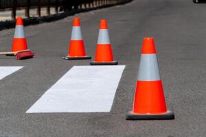 Bright orange traffic cones are placed along a newly marked crosswalk in an urban setting, directing pedestrians and ensuring safety in the area photo