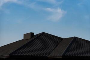 The roof of a suburban house is visible against a bright blue sky with wispy clouds. The textured tiles create a distinct pattern, enhancing the architectural features photo