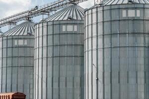 The view features several towering metallic grain silos set against a clear blue sky, highlighting their role in agricultural storage and production photo