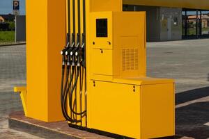The bright yellow dispenser, featuring multiple hoses, is positioned at a gas station during the day, ready for vehicles to refuel conveniently photo
