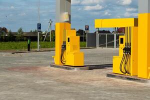A bright, modern fuel station features yellow pumps set in a spacious, open area under a clear blue sky. Nearby parking spaces are visible, enhancing accessibility photo