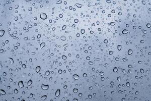 Many small raindrops are scattered across a smooth, gray surface, creating a textured and abstract pattern photo