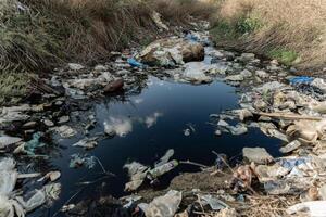 A polluted stream filled with plastic debris reflects the sky, showing the impact of trash on natural water bodies, emphasizing urgent environmental concerns photo
