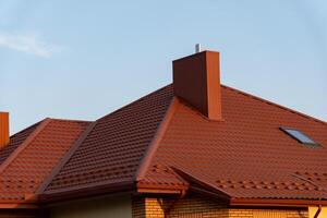 The vibrant red roof structure features a prominent chimney and an angled design, bathed in warm afternoon light against a clear blue sky, highlighting its architectural details photo