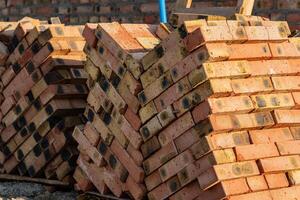 Piles of orange and brown bricks rest against a blurred backdrop at a construction site, suggesting preparation for upcoming building projects under bright sunlight photo