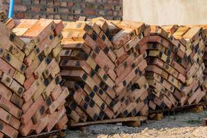A large pile of stacked bricks arranged neatly at a construction site under bright daylight, showcasing the materials for upcoming building efforts in an urban environment photo