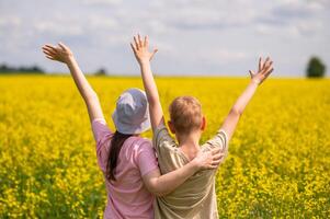 Happy children with raised hands enjoying summer in a blooming yellow rapeseed field, back view photo