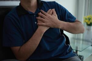 man is holding his chest while sitting on a couch photo