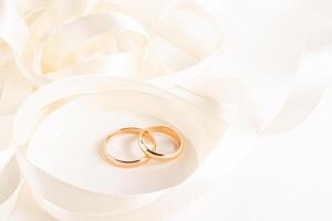 Two gold wedding rings lie inside a beautiful twisted satin ribbon on a beige silk fabric. Mockup for wedding design, cards, invitations. photo