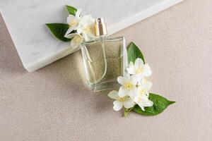An elegant perfume bottle leans on a white marble podium with jasmine flowers. A blank bottle mockup. Fragrance presentation. beige stone background. photo