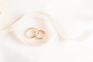 Two gold wedding rings lie inside a beautifully twisted beige ribbon on a satin background. top view. A copy space. presentation of wedding rings photo