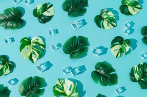 Summer day scene with ice cubes and tropical monstera leaves on blue background. Sun and shadows. Summertime pattern concept. Flat lay style wallpaper. Top view banner. Summer aesthetic backdrop. photo