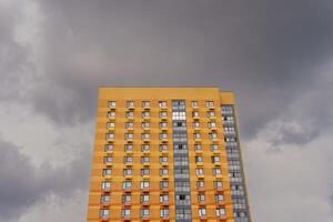An orange tall building with windows against the background of gloomy clouds. The atmosphere of approaching trouble. photo