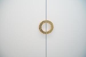 golden round handle on white cabinet doors. the handle has a rounded shape, ribbed structure. space for text photo