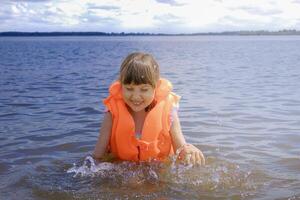 Child in bright life vest splashes water while playing in lake photo