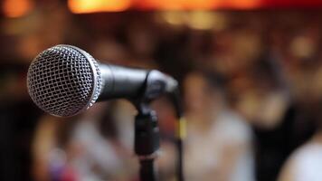 Close-Up Of Microphone On Stage With Blurred Audience In Background, Symbolizing Public Speaking, Performance, Or Live Presentation Atmosphere video