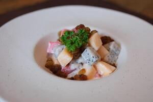 fruit salad with melon watermelon white precious fruit and raisins topped with yogurt on a white deep plate photo