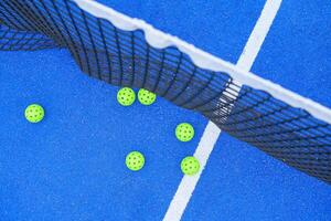 six pickleball balls near the net in a blue court, top down view photo