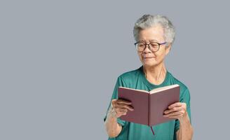 Senior woman is reading a book while standing on a gray background photo