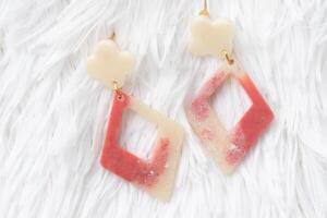 Geometric dangle earrings with cream and red marbled resin, featuring flower and diamond shapes, displayed on soft white fur background, modern and stylish accessory photo