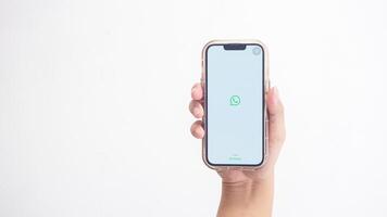 Yogyakarta, Indonesia, 2025 - Hand holding phone that shows front page of WhatsApp application, a communication platform, on the screen isolated on white background photo